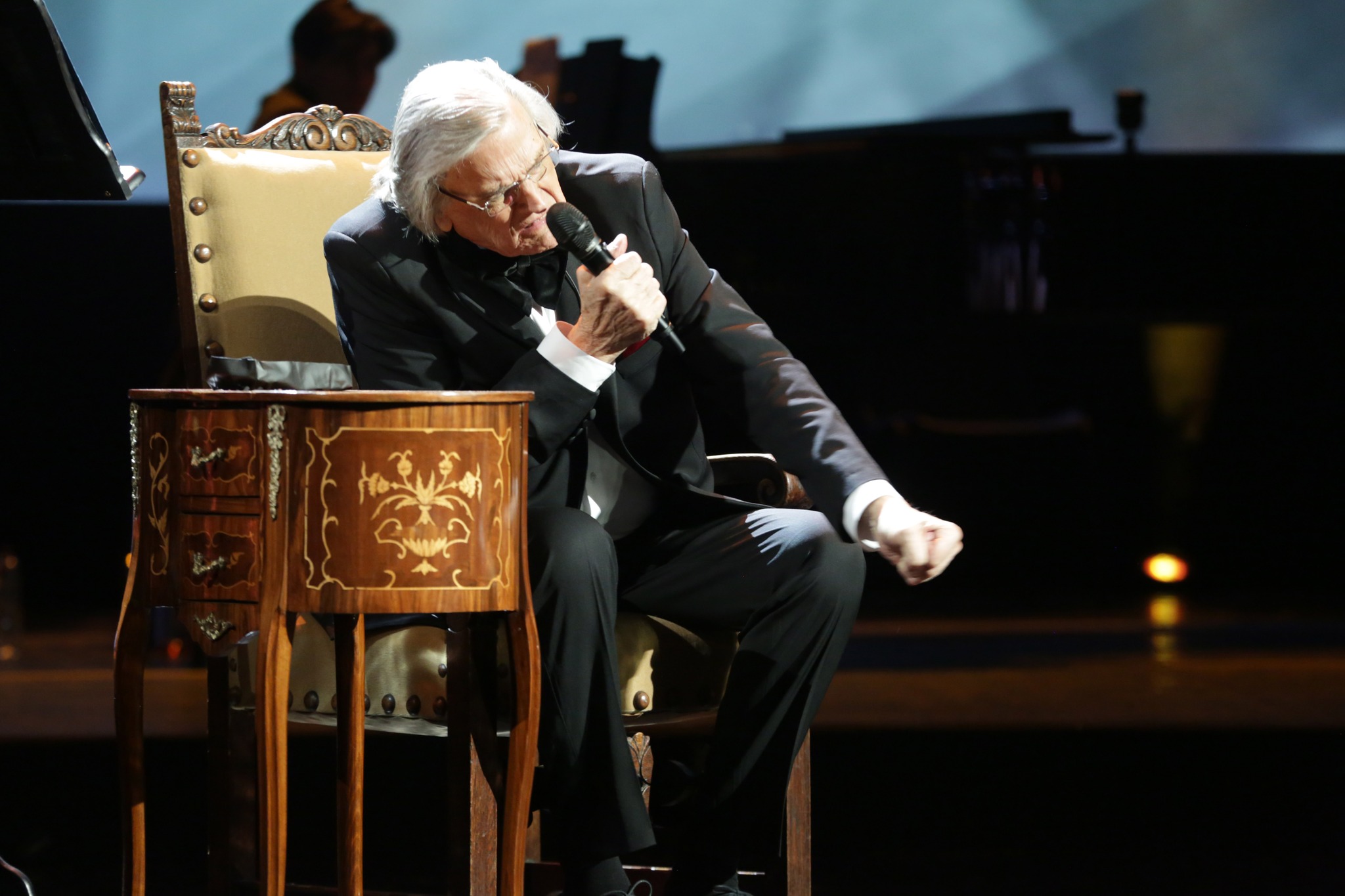 Florin Piersic, &icirc;n costum negru, elegant, st&acirc;nd pe un fotoliu pe scenă, la spectacolul aniversar, de c&acirc;nd a &icirc;mplinit 90 de ani