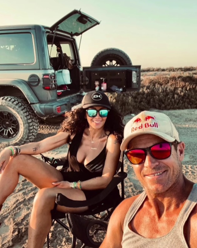 Mihaela Rădulescu și Felix Baumgartner st&acirc;nd &icirc;mpreună pe două scaune pliabile, pe o plajă sălbatică, l&acirc;ngă o mașină de teren, purt&acirc;nd ochelari de soare și fotografiindu-se &icirc;mpreună