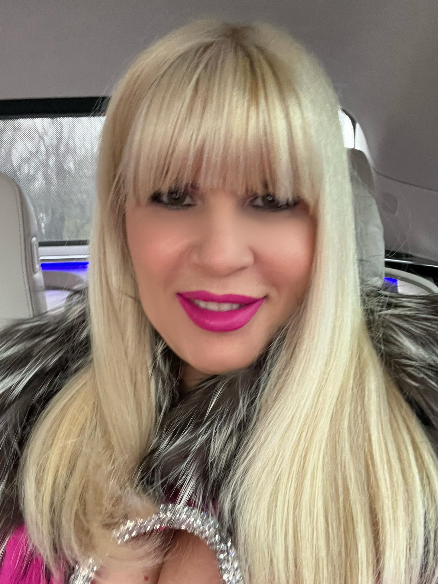 Elena Udrea &icirc;n mașină, cu o haină de blană pe umeri, &icirc;n timp ce pe dedesubt poartă o rochie roz, cu decolteu ad&acirc;nc, conturat de pietre strălucitoare