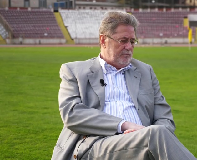 Cornel Dinu &icirc;n costum și cămașă pe stadion, st&acirc;nd pe scaun, &icirc;n fața unei discuții cu Mircea Lucescu