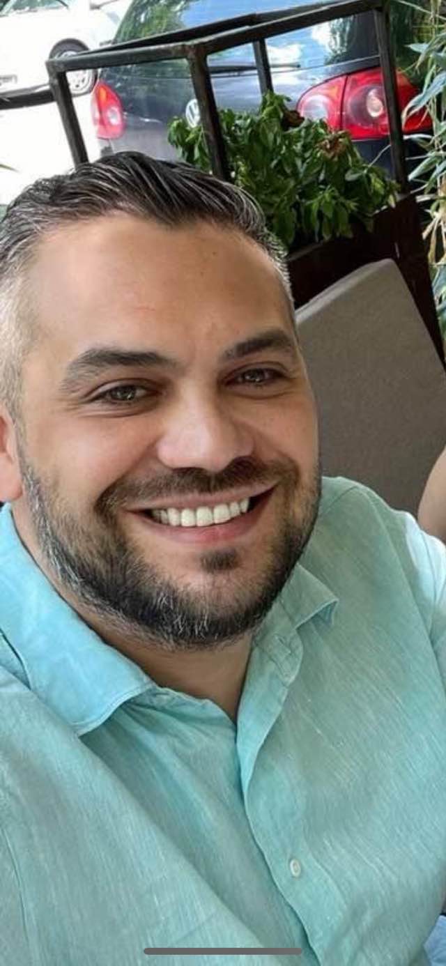 Creatorul de modă Eugen Olteanu z&acirc;mbitor, făc&acirc;ndu-și un selfie &icirc;ntr-o cămașă bleu, &icirc;n timp ce stătea la masă