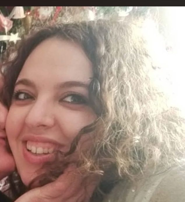 Anna&nbsp;Democrito z&acirc;mbitoare, cu părul creț și machiată subtil, cu ochii conturați cu un creion negru