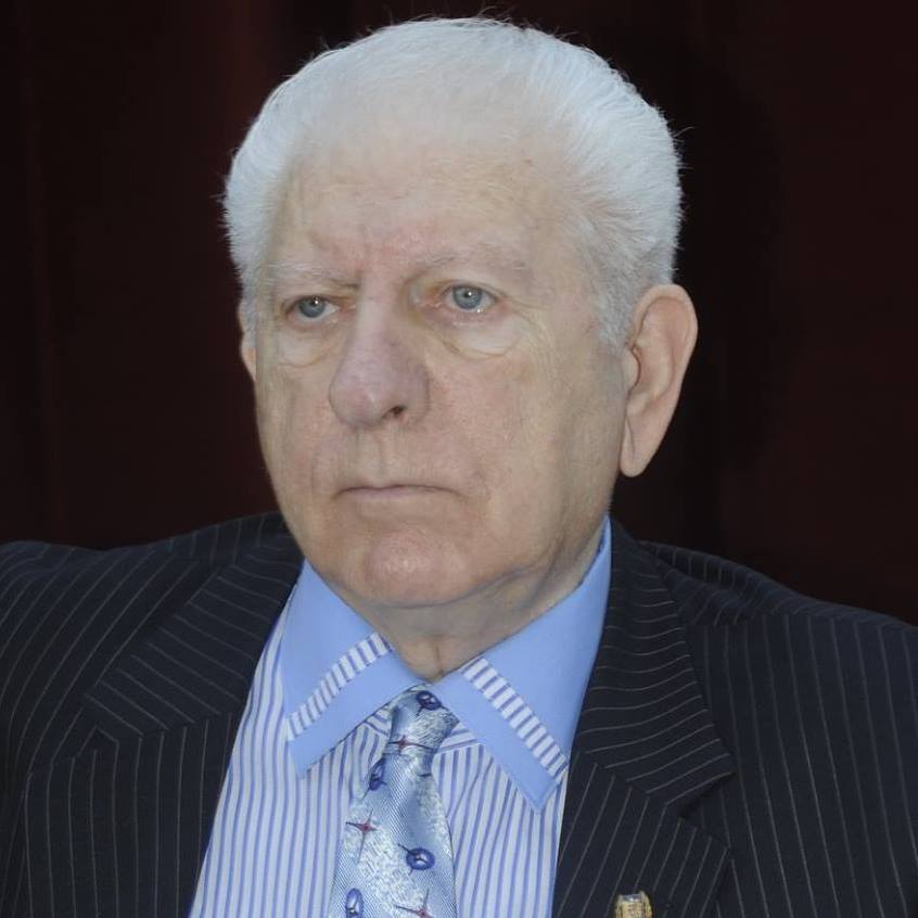 Dan Claudiu Tănăsescu &icirc;n sacou negru cu dungi albe, cămașă albă cu dungi bleu și cravată bleu cu imprimeuri diverse