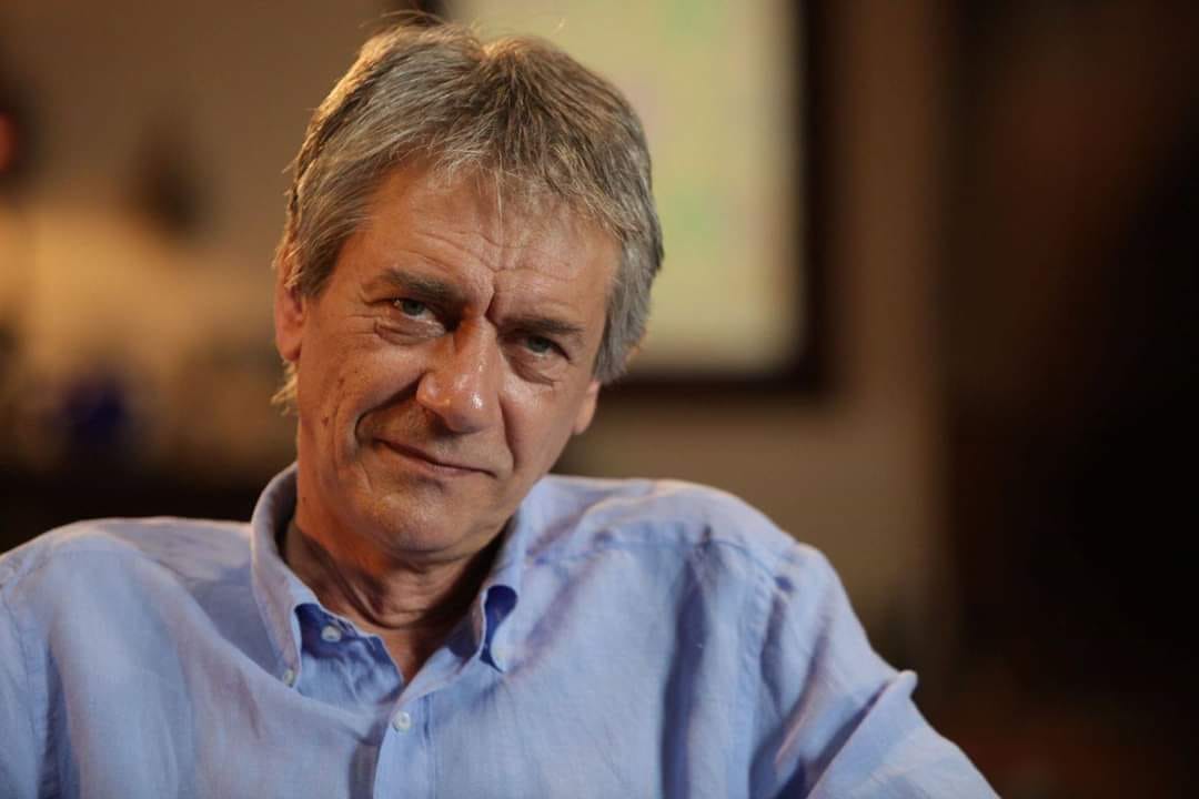 Marcel Iureș st&acirc;nd pe un fotoliu, &icirc;n cămașă bleu, privind fix spre obiectivul camerei de fotografiat