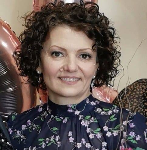 Florentina Bolojan brunetă, cu părul creț, z&acirc;mbitoare, &icirc;ntr-o rochie neagră cu flori roz