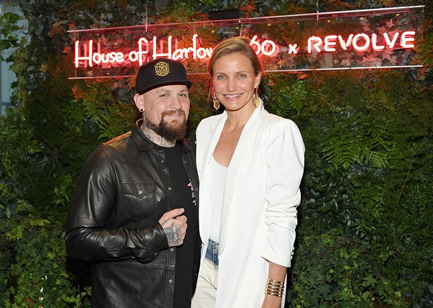 Cameron Diaz și soțul ei, Benji Madden, fotografiindu-se &icirc;mpreună la un eveniment, la foto cornerul făcut din plante verzi și litere luminoase, &icirc;mbrăcați &icirc;n alb și negru