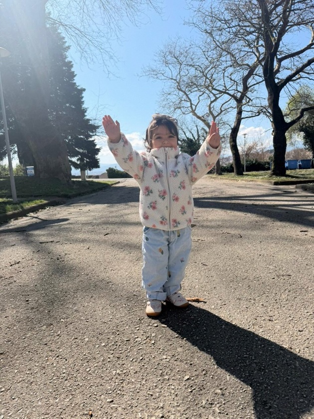Nepoata lui Damian Drăghici &icirc;n blugi și o jachetă albă cu imprimeu floral, surprinsă &icirc;n poză &icirc;n timp ce ținea m&acirc;inile ridicate.