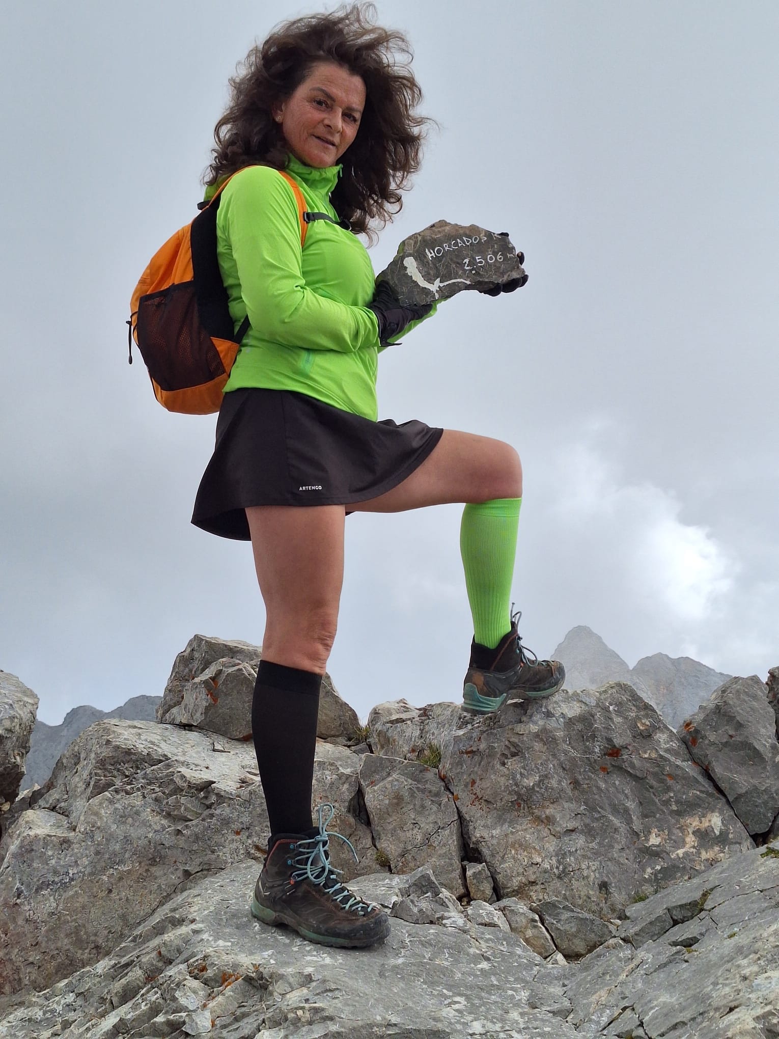 Alpinista Cristina Dinu pe munte, &icirc;mbrăcată &icirc;n echipament sport, țin&acirc;nd &icirc;n m&acirc;nă o piatră pe care scrie altitudinea p&acirc;nă la care a urcat