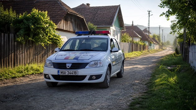 Mașină de poliție care staționează pe o stradă, &icirc;ntr-o zonă rurală, l&acirc;ngă un gard de lemn