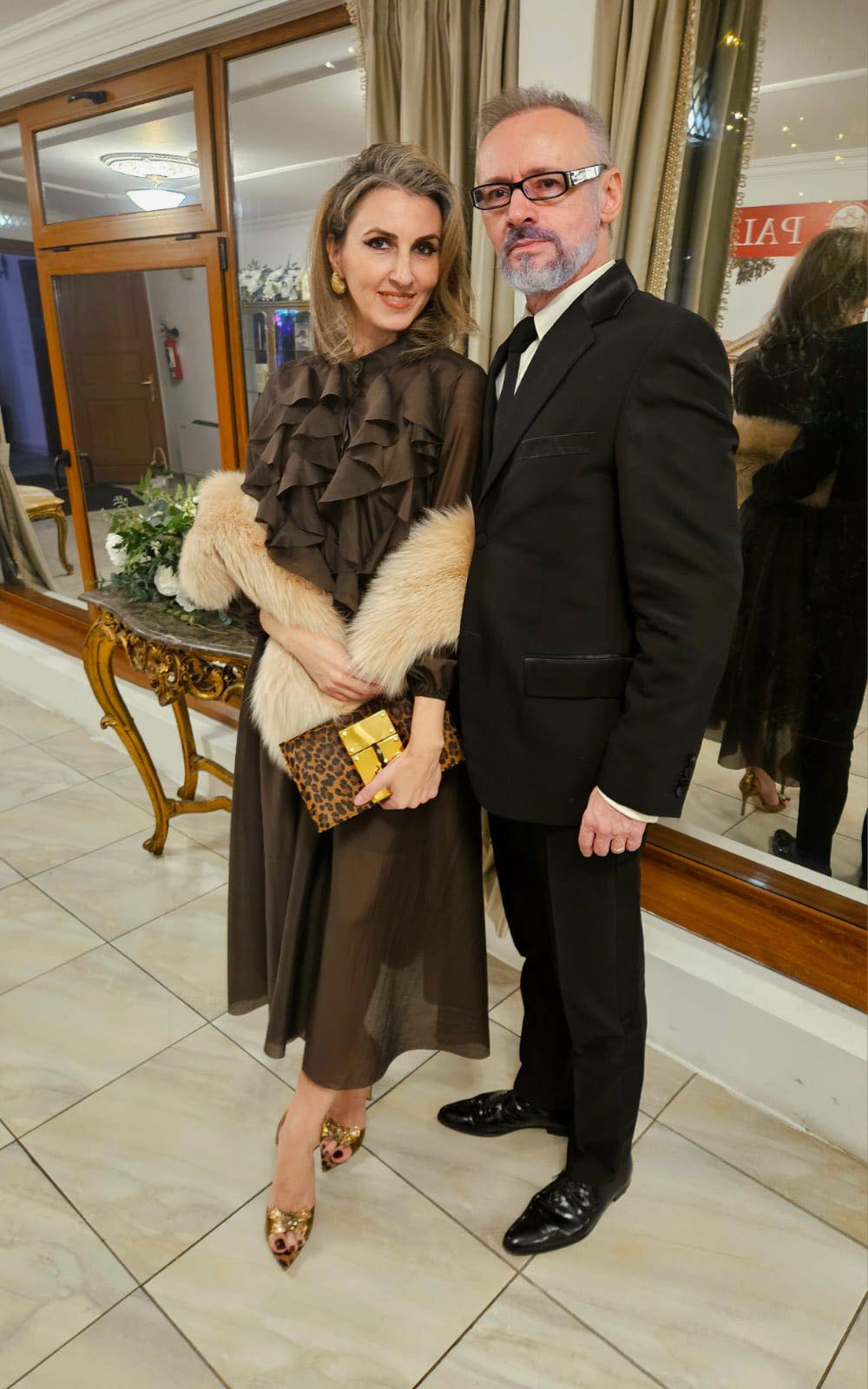 Mihai Albu alături de soția sa Elena, &icirc;mbrăcați elegant, el &icirc;n costum negru și ea &icirc;ntr-o rochie maro, cu o blană bej pe umeri și pantofi aurii &icirc;n picioare