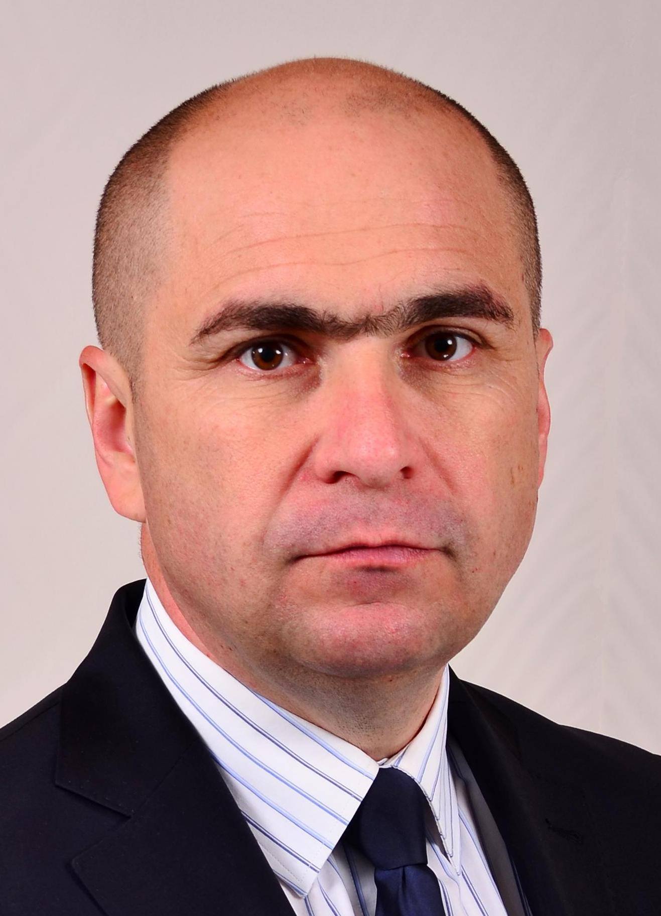 Ilie Bolojan c&acirc;nd era mai t&acirc;năr, &icirc;mbrăcat sacou negru, cămașă albă cu dungi și purt&acirc;nd o cravată bleumarin