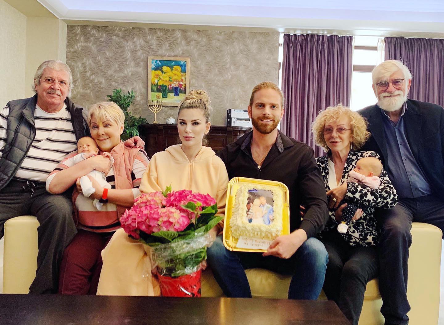Tablou de familie cu Alina și Ilan Laufer alături de gemenii lor nou-născuți și de părinții lor, sărbătorind &icirc;mpreună cu tort și flori