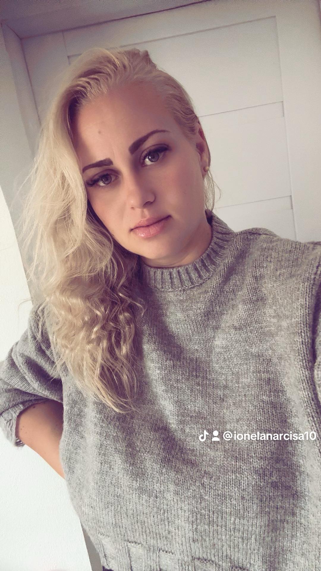 Ioana Narcisa făcându-și un selfie în timp ce ținea o mână în șold și era îmbrăcată într-un pulover gri