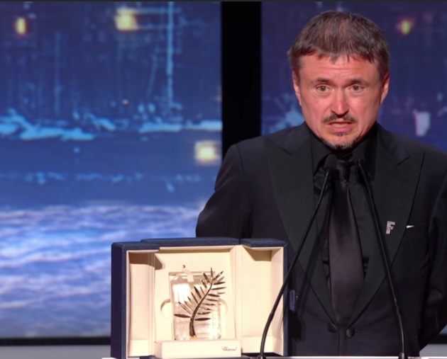 Cristian Mungiu &icirc;mbrăcat complet &icirc;n negru, la Festivalul de Film de la Cannes, av&acirc;nd &icirc;n față premiul Palme d'Or, obținut pentru filmul &bdquo;Fjord&rdquo;