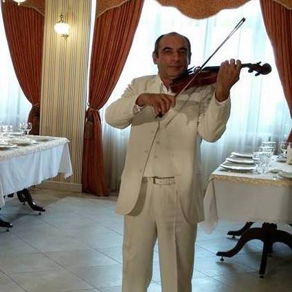 dirijorul&nbsp;Adrian Luca, &icirc;mbrăcat &icirc;ntr-un costum bej, c&acirc;nt&acirc;nd la vioară