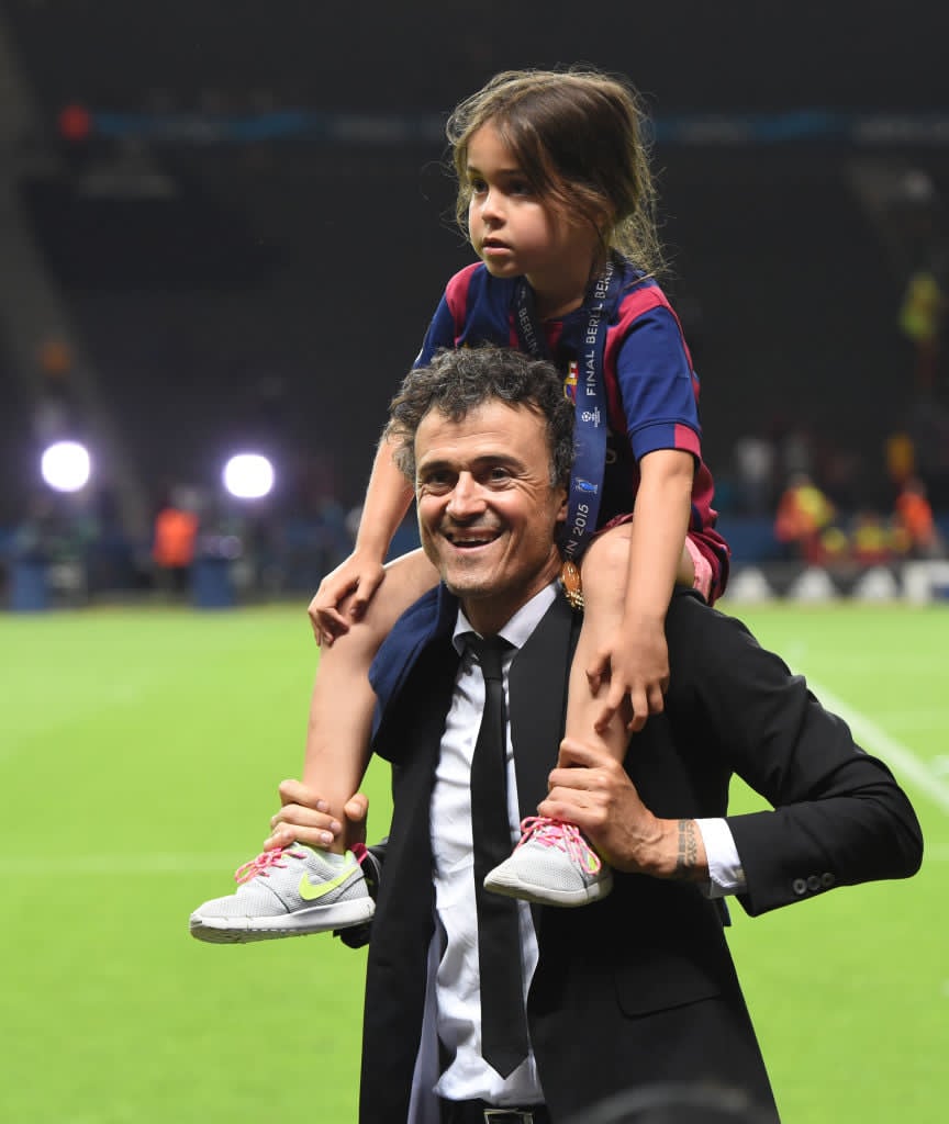 Luis Enrique z&acirc;mbitor, &icirc;n costum, pe terenul de fotbal, țin&acirc;nd-o pe umeri pe fiica sa, Xana, care poartă la g&acirc;t medalia c&acirc;știgată de echipa lui