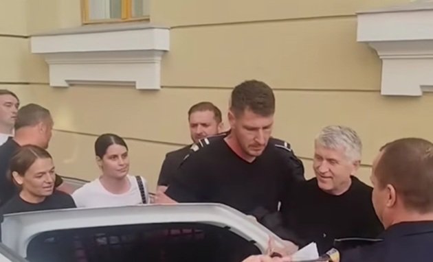 Cristian Pomohaci z&acirc;mbitor, &icirc;mbrăcat &icirc;n negru, &icirc;n timp ce era băgat &icirc;n mașină de polițiști, la Tribunalul Mureș