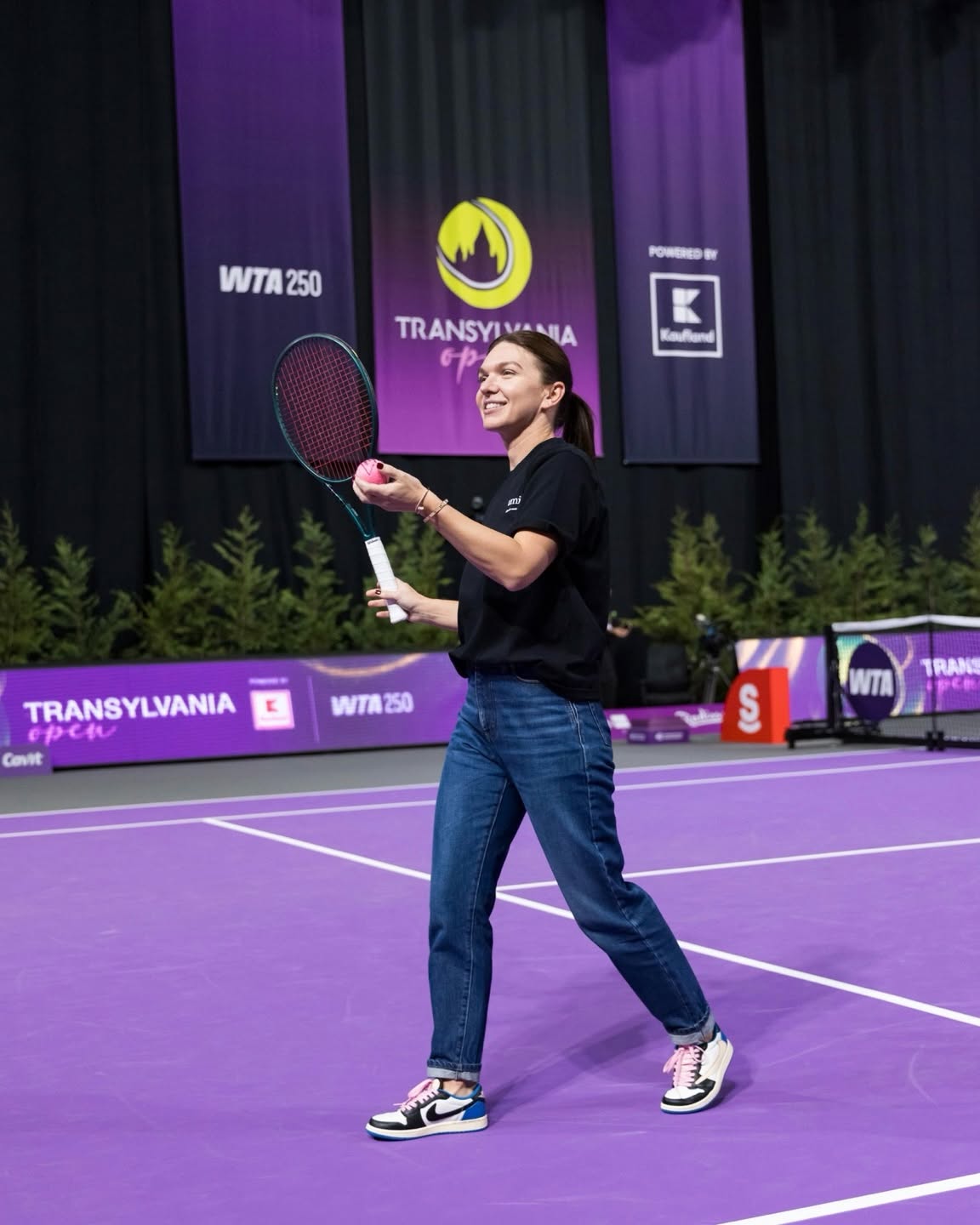 Simona Halep pe terenul de tenis, cu mingea și paleta &icirc;n m&acirc;nă, &icirc;mbrăcată lejer, &icirc;n blugi și tricou negru