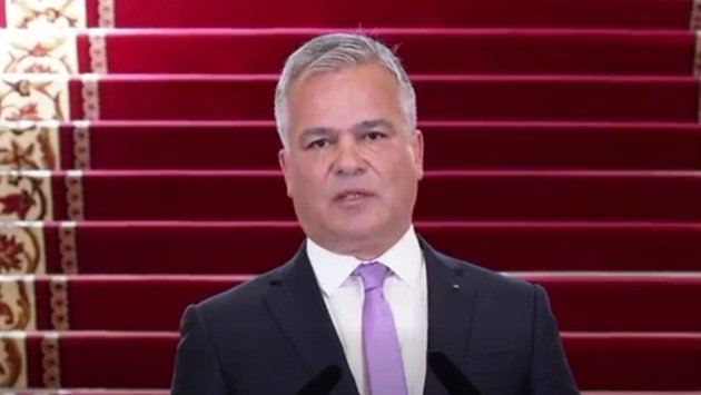 Adrian Veștea vorbind la o conferința de presă de la Palatul Cotroceni, &icirc;mbrăcat &icirc;n costum &icirc;nchis la culoare, cu cămașă albă și cravată lila