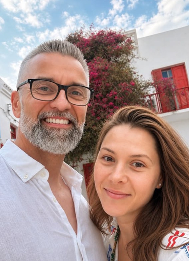 Oksana Ionașcu făc&acirc;nd o fotografie &icirc;n timp ce se afla undeva afară l&acirc;ngă soțul ei, Cezar Ionașcu, &icirc;n timp ce &icirc;n spatele lor se vedea cerul și o clădire acoperită cu flori roz
