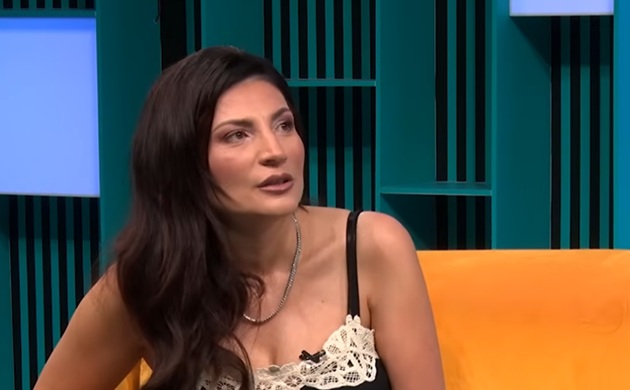 Ioana Ginghină st&acirc;nd pe o canapea portocalie, &icirc;ntr-un platou de televiziune, &icirc;mbrăcată &icirc;ntr-un maiou negru, cu flori albe din dantelă
