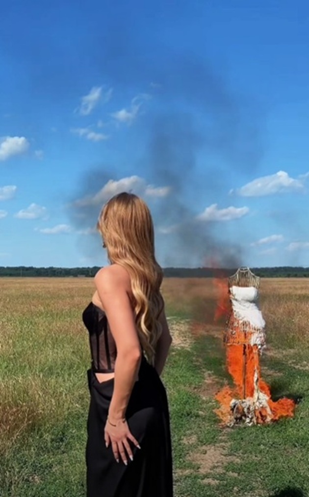 Codruța Filip pe un c&acirc;mp, privind  o rochie de mireasă cum arde pe un manechin