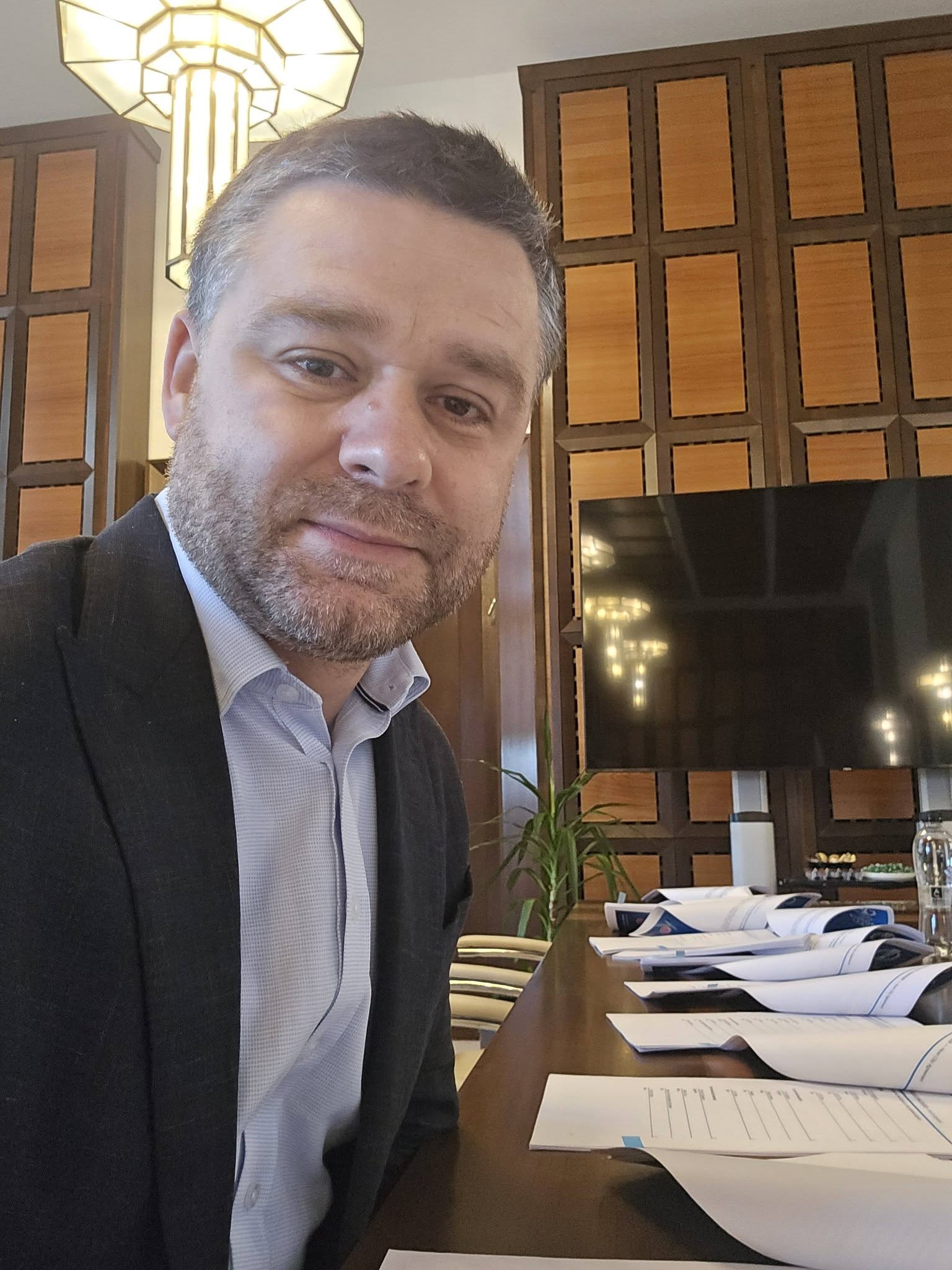 Ciprian Ciucu st&acirc;nd la o masă lungă, &icirc;ntr-o sală de ședință, aștept&acirc;ndu-și colegii politicieni