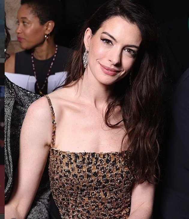 Anne Hathaway &icirc;ntr-o rochie cu auriu și negru, cu bretele, &icirc;n timp ce &icirc;și ținea părul pe o parte pentru a i se vedea cercelul argintiu de mari dimensiuni