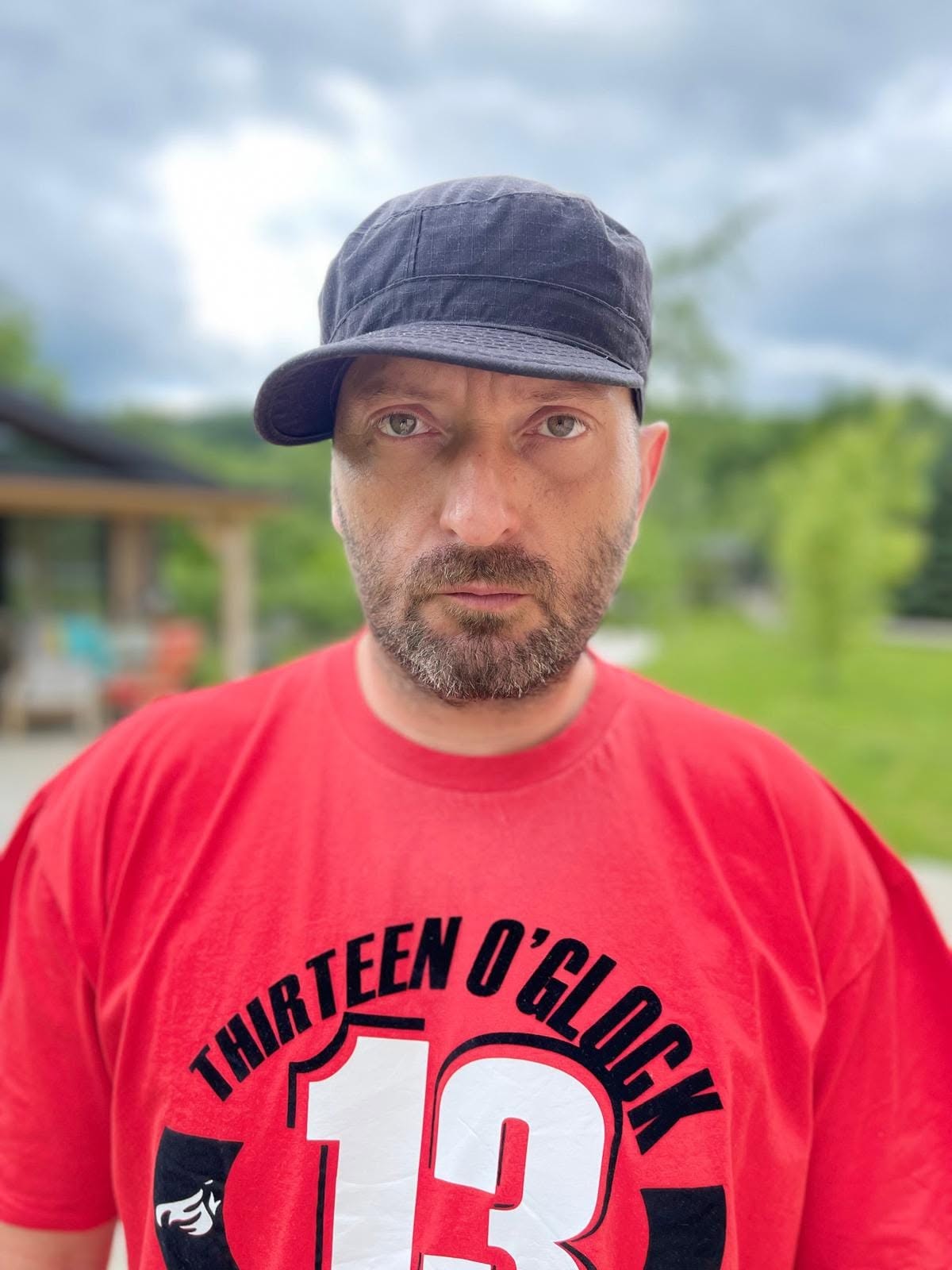 Cheloo cu șapcă pe cap, &icirc;mbrăcat &icirc;ntr-un tricou roșu cu imprimeu tip text