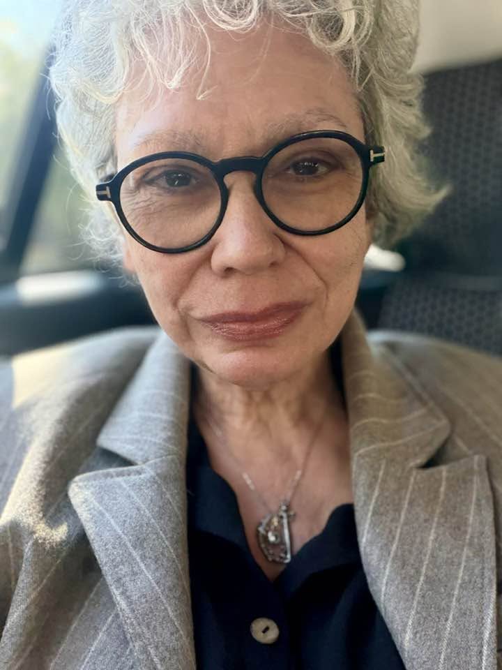 Oana Pellea &icirc;ntr-o cămașă bleumarin și sacou gri deschis cu dungi albe, purt&acirc;nd ochelari de vedere de mari dimensiuni și un colier argintiu la g&acirc;t, făc&acirc;ndu-și un selfie &icirc;n timp ce se afla &icirc;ntr-o mașină