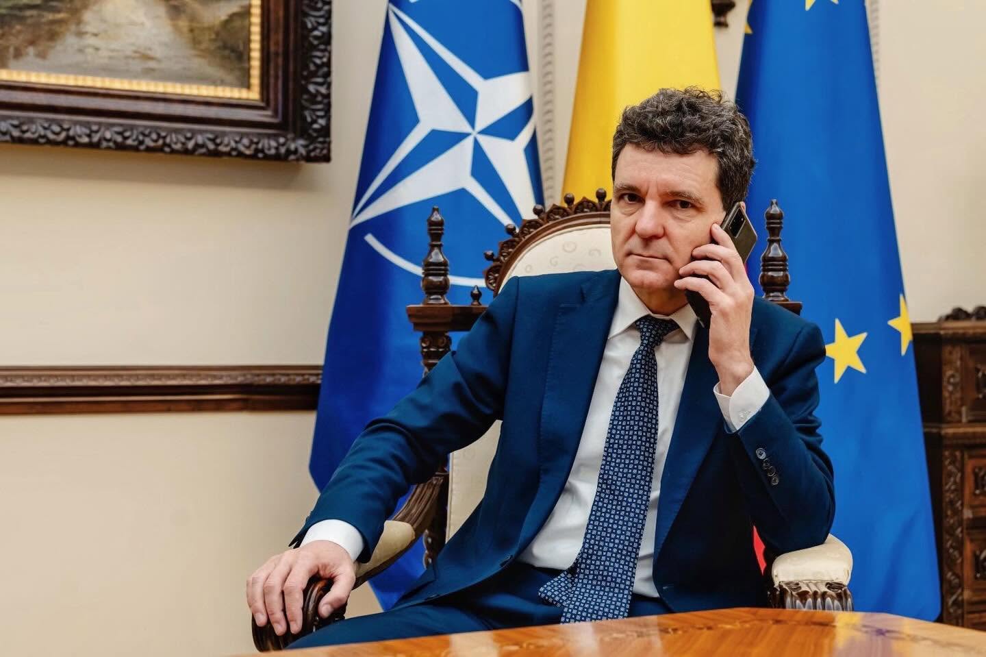 Nicușor Dan st&acirc;nd la birou, &icirc;n scaunul de președinte, vorbind la telefon, &icirc;n timp ce &icirc;n fundal se văd trei steaguri, cel al NATO, cel al Rom&acirc;niei și cel al Uniunii Europene.