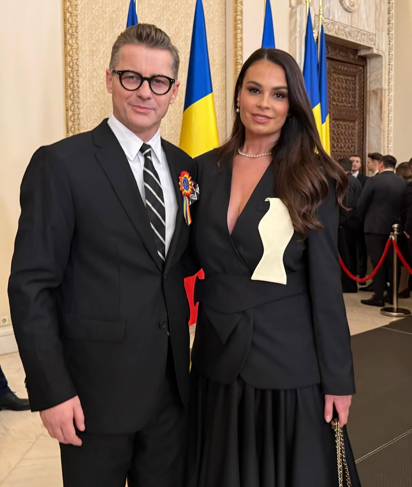 Adrian S&icirc;nă și Anca Serea la Palatul Cotroceni, &icirc;mbrăcați am&acirc;ndoi asortat, &icirc;n negru, &icirc;n timp ce artistul avea &icirc;n piept o insignă &icirc;n culorile steagului Rom&acirc;niei