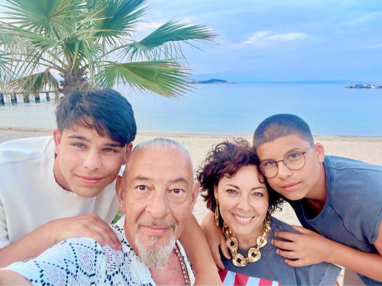 Bodo de la Proconsul și soția sa Loredana, alături de băieții lor Filip și Daniel, st&acirc;nd toți patru &icirc;mbrățișați pe o plajă &icirc;n Grecia, cu marea pe fundal