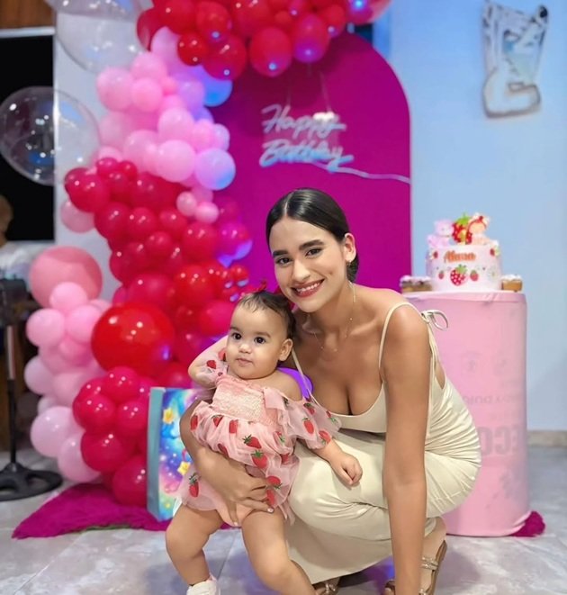 Andrea, soția fotbalistului H&eacute;ctor Bello, alături de fiica lor Alana, la aniversarea acesteia, l&acirc;ngă tort și panoul foto cu baloane