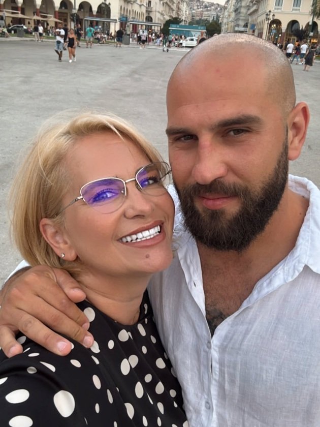 Dan Giuvelic &icirc;ntr-o cămașă albă, țin&acirc;nd-o de g&acirc;t pe Paula Chirilă, care z&acirc;mbește larg și este &icirc;mbrăcată cu o rochie neagră cu buline