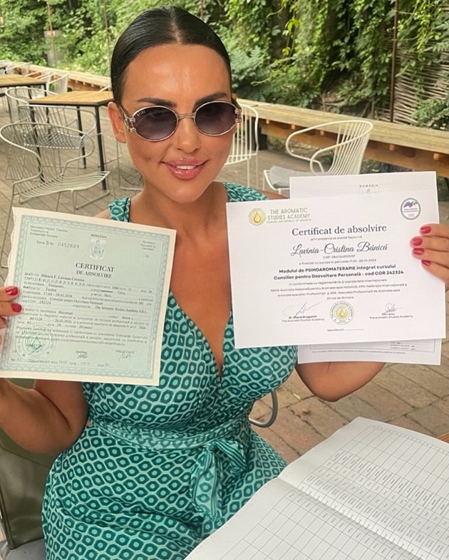 Lavinia Pîrva într-o rochie verde cu romburi, la o terasă, ținând în mână diplomele de absolvire ale cursului pe care l-a făcut, în timp ce purta ochelari de soare la ochi