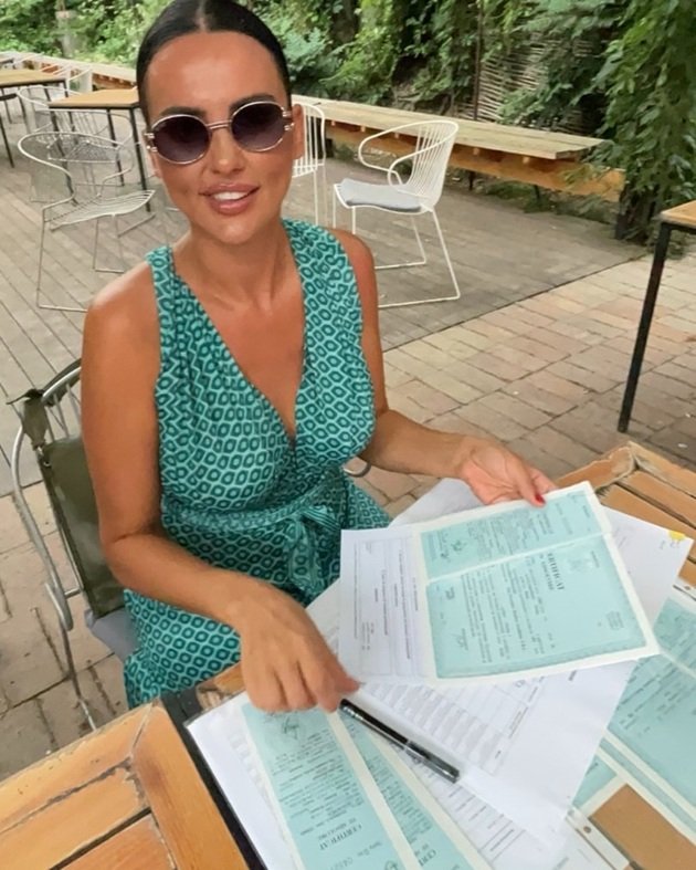 Lavinia Pîrva cu ochelari de soare, într-o rochie verde cu romburi, semnându-și diplomele primite în urma absolvirii unor cursuri