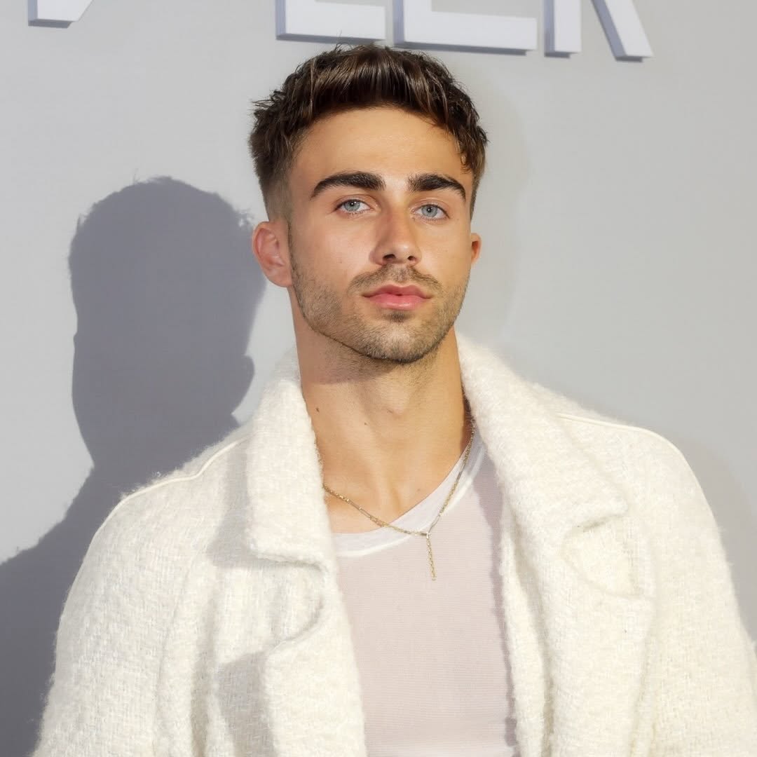 Mustățea Alberto, dansatorul Andreei Bălan, &icirc;mbrăcat &icirc;ntr-un tricou alb, cu un cardigan alb pufos pe deasupra, purt&acirc;nd la g&acirc;t un lanț auriu