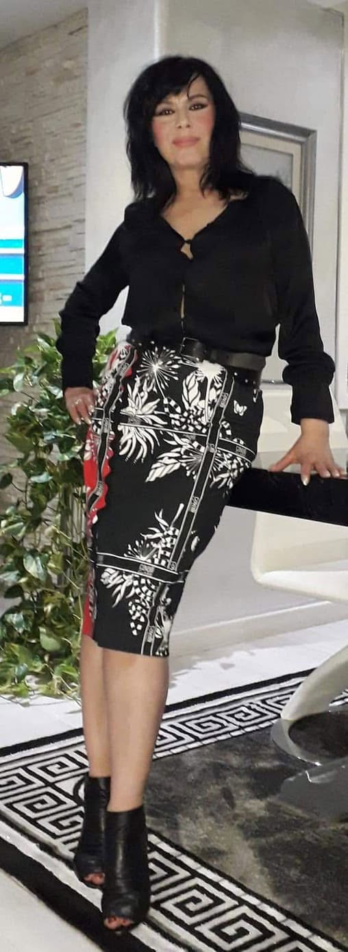 Mariana Moculescu &icirc;mbrăcată &icirc;n negru și alb, &icirc;n bluză cu m&acirc;necă lungă și fustă creion, pe tocuri, st&acirc;nd sprijinită de o masă