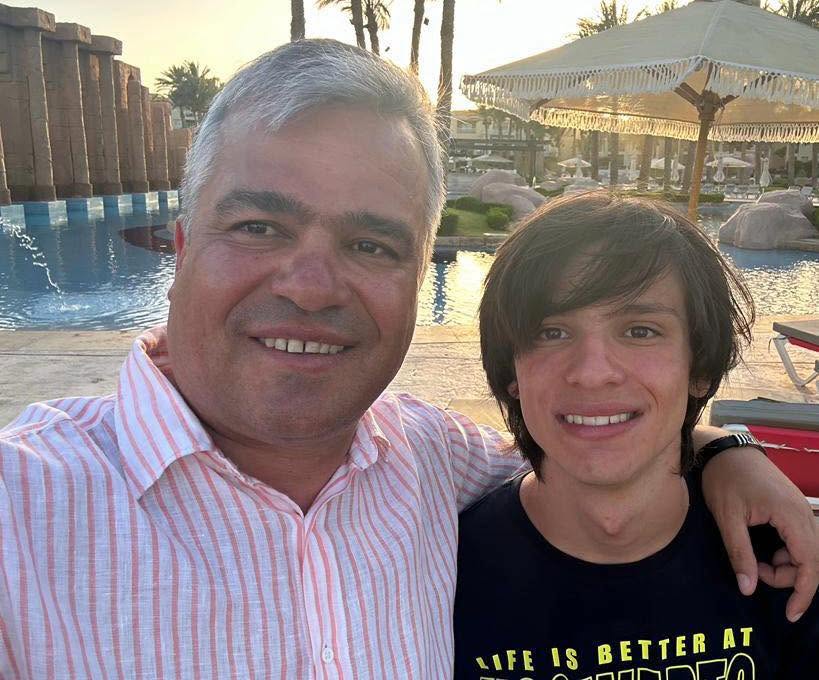 Adrian Veștea alături de fiul său cel mic, Daniel, pe care &icirc;l ține de g&acirc;t la apus, l&acirc;ngă o piscină &icirc;nconjurată de șezlonguri și umbrele cu franjuri