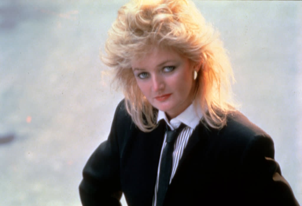 Bonnie Tyler, &icirc;n tinerețe, cu părul aranjat cu volum, &icirc;mbrăcată &icirc;ntr-o cămașă albă cu dungi negre și un sacou negru, purt&acirc;nd o cravată neagră