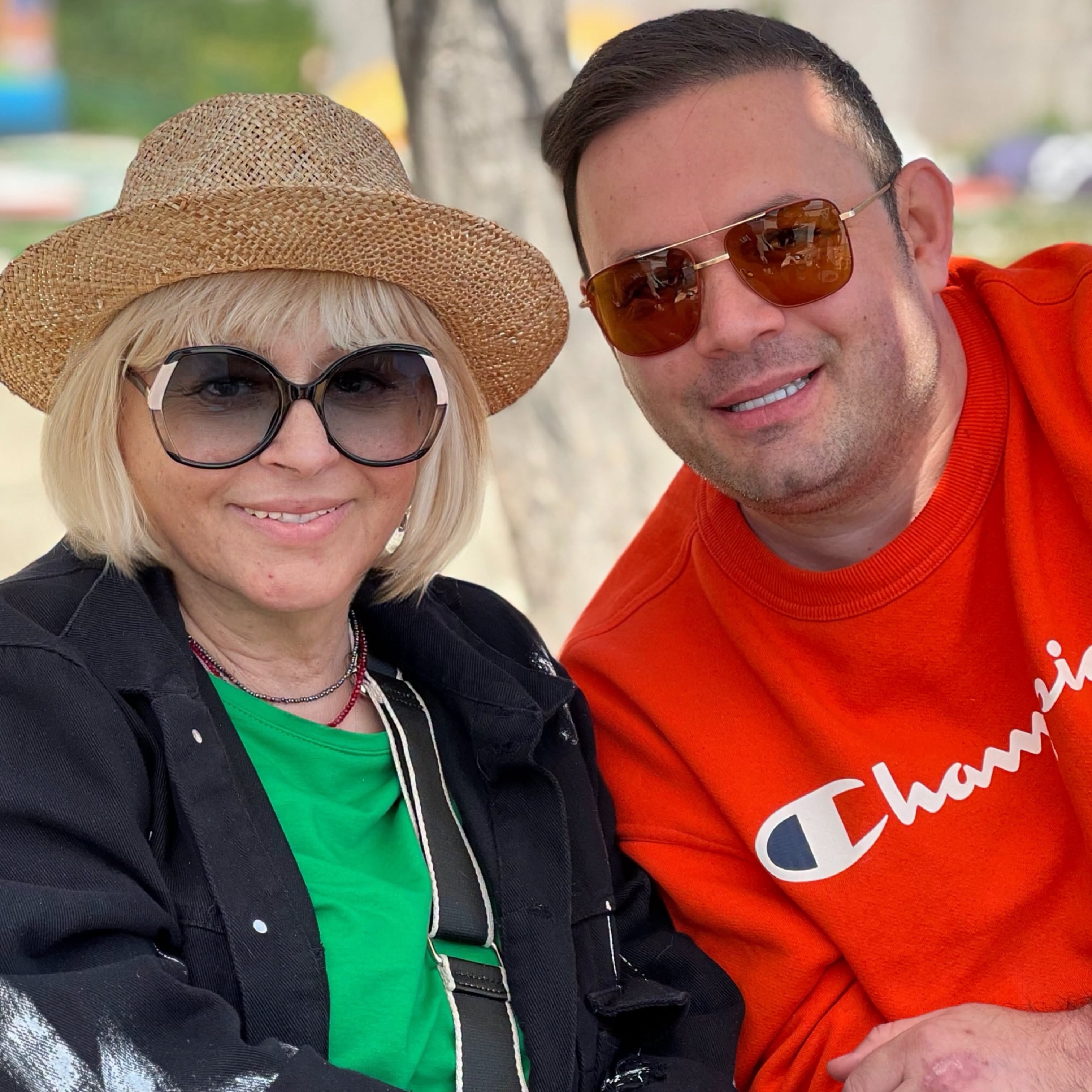 Mirabela Dauer într-un tricou negru, cu o jachetă neagră, purtând pe cap o pălărie de paie și ochelari de soare la ochi, stând lângă Raoul, care de asemenea purta ochelari de soare și era îmbrăcat într-o bluză roșie