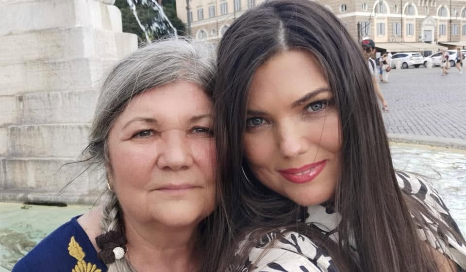 Paula Seling și mama ei, fotografiindu-se st&acirc;ns prijinită una de cealaltă l&acirc;ngă o statuie, &icirc;n centrul unui oraș
