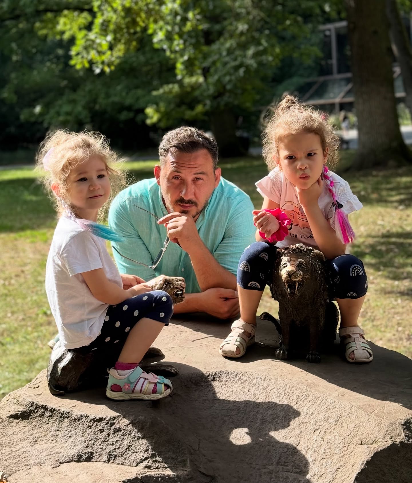 Ștefan Stan &icirc;n parc, alături de fiicele lui, Elif și Mira, care stăteau pe un monument cu animale