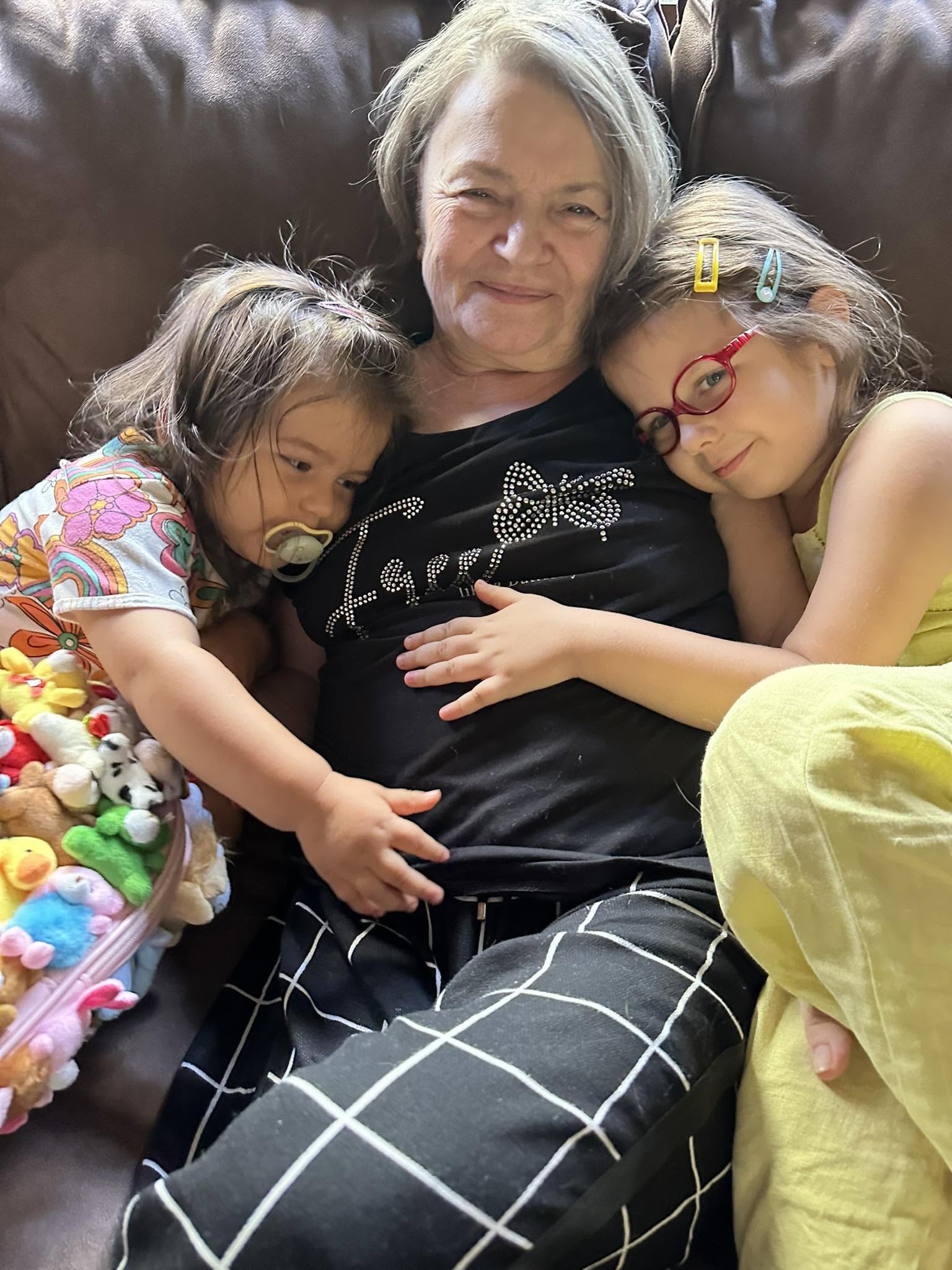 Mama lui Codin Maticiuc alături de fiicele acestuia care o țin ăn brațe și &icirc;și țin capetele pe pieptul ei, &icirc;n timp ce stau toate trei pe o canapea