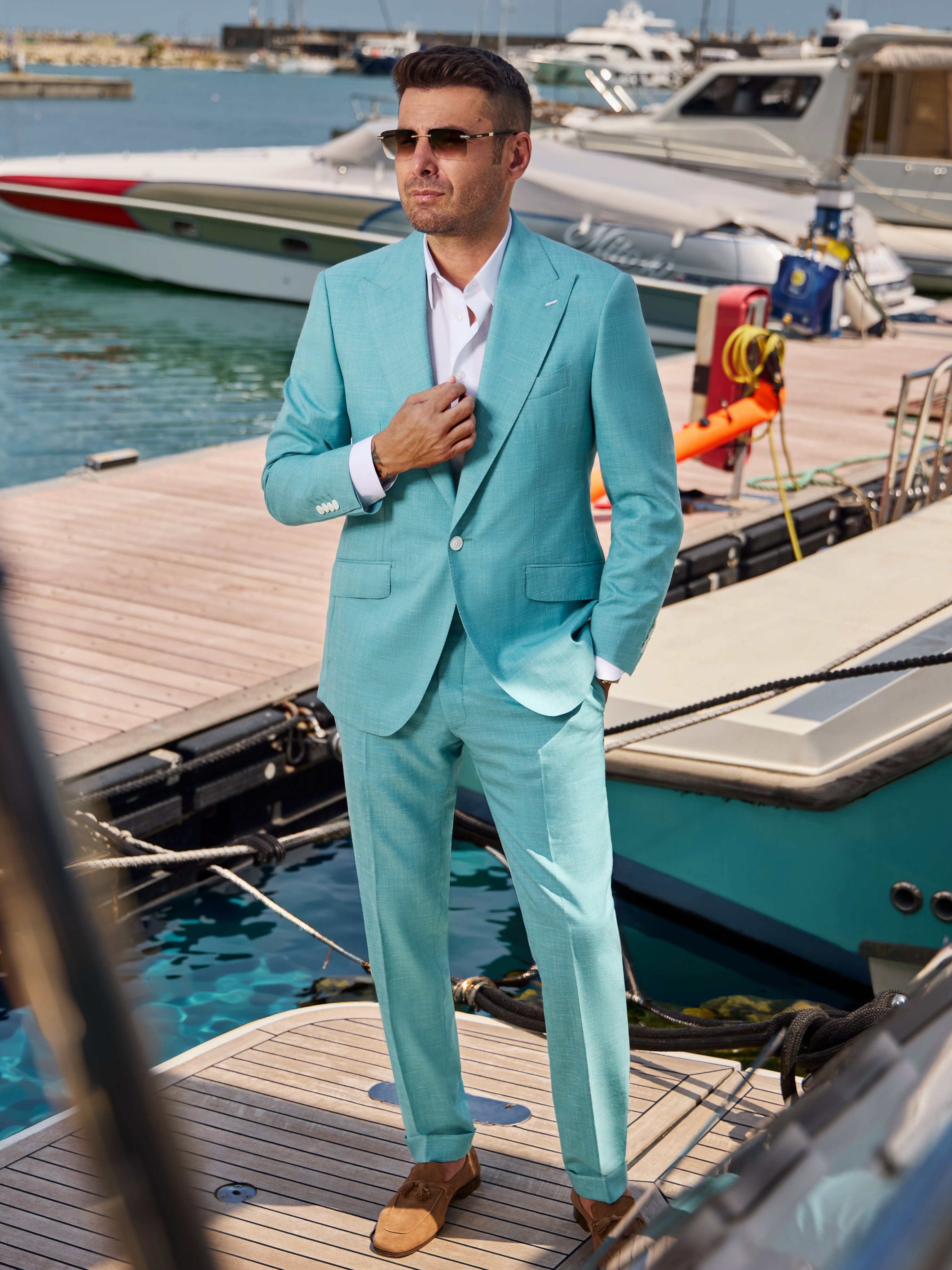 Adrian Mutu &icirc;ntr-un costum bleu, cu ochelari de soare, st&acirc;nd pe un ponton, &icirc;ntr-un port, &icirc;nconjurat de mai multe bărci
