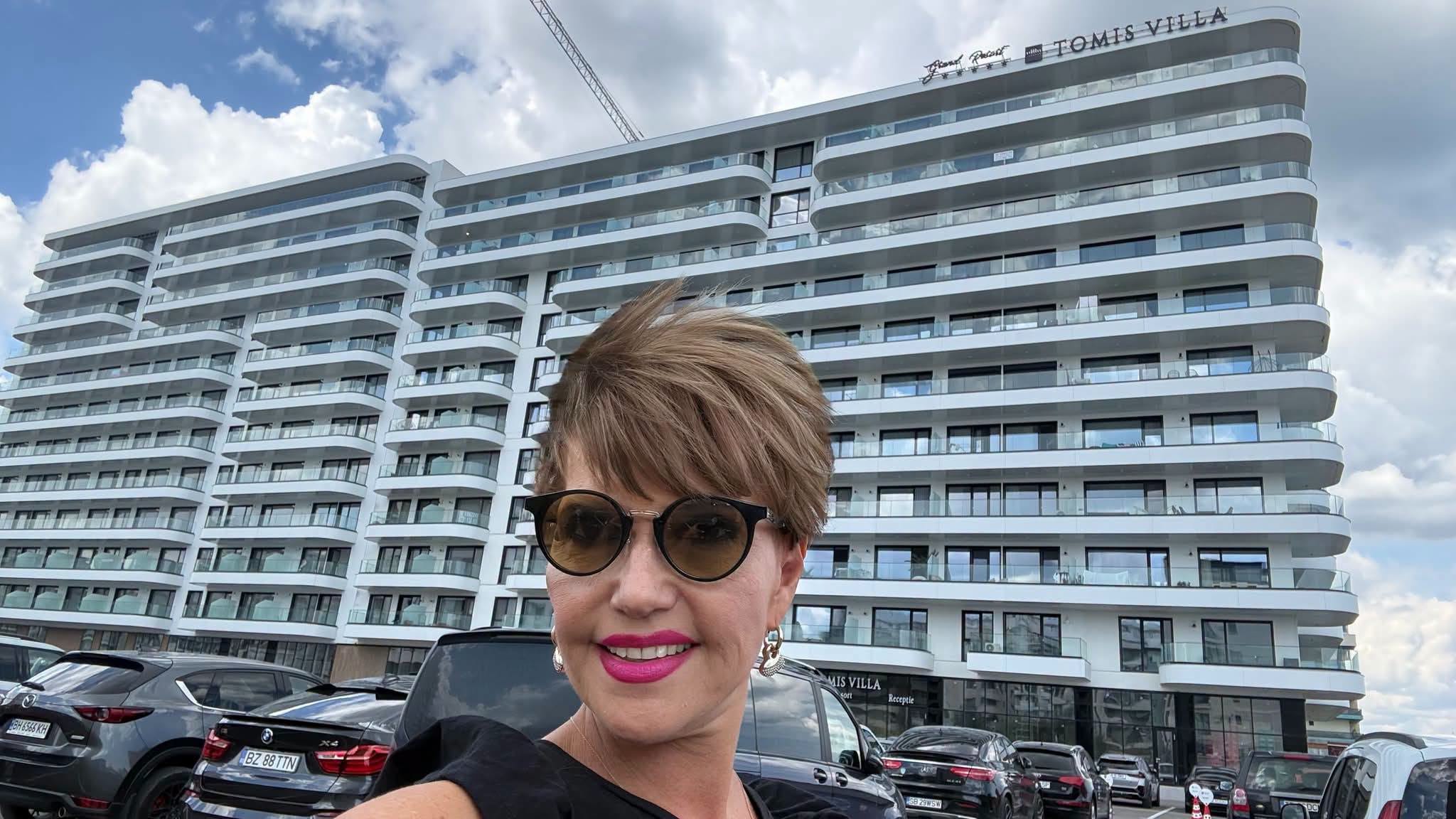 Marina Almășan zâmbitoare, cu ochelari de soare, făcându-și un selfie în fața blocului de la mare în care logodnicul ei a cumpărat un studio