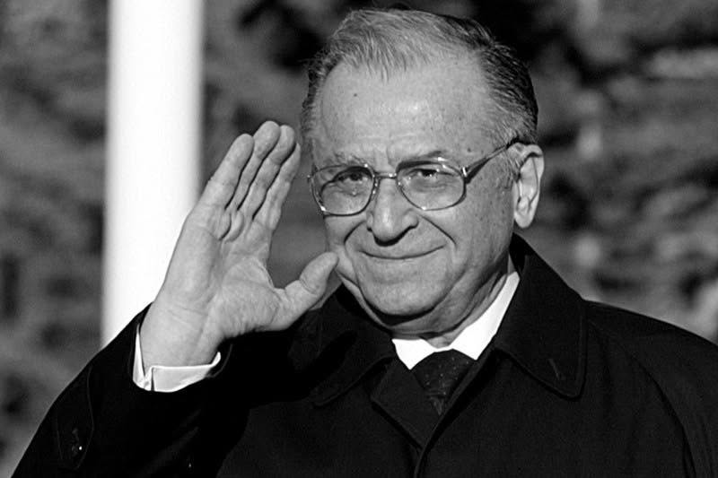 Imagine alb-negru cu Ion Iliescu salut&acirc;nd cu m&acirc;na, &icirc;n timp ce purta un pardesiu negru, pe sub car avea cămașă albă și cravată cu picățele