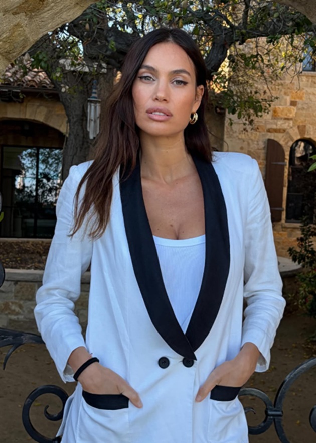 Alina Pușcău &icirc;ntr-un sacou alb cu rever negru și nasturi negri, țin&acirc;ndu-și m&acirc;inile &icirc;n buzunar