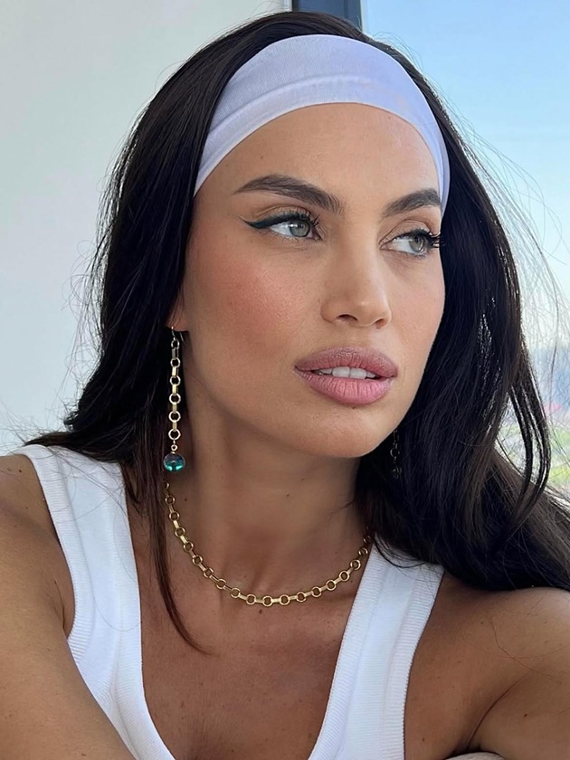 Modelul Alina Pușcău privind &icirc;n lateral, &icirc;ntr-un top alb, cu bentiță albă pe cap, purt&acirc;nd bijuterii aurii de mari dimensiuni